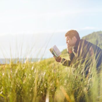man reading book on beach near lake during daytime